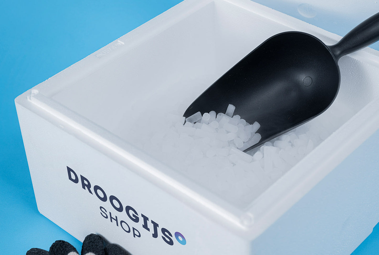 Droogijs polystyrene box with 5kg dry ice pellets and black scoop on blue background.